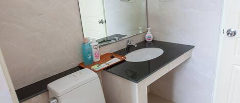 Une salle de bain équipée de toilettes, d’un lavabo, d’un miroir et d’une poubelle.