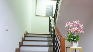 Una escalera con escalones de madera y barandilla metálica, una mesita con planta en maceta, y un cuadro enmarcado en la pared.