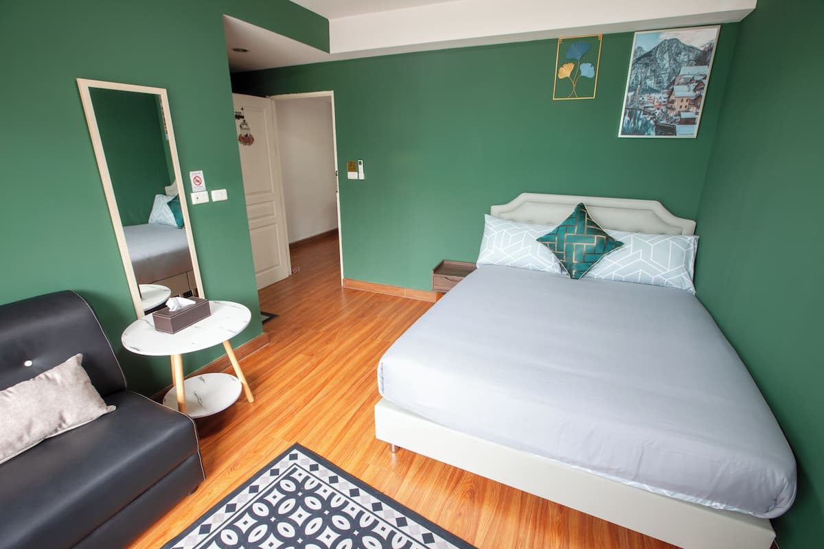 A bedroom with a bed, a sofa, a small table, and a mirror.