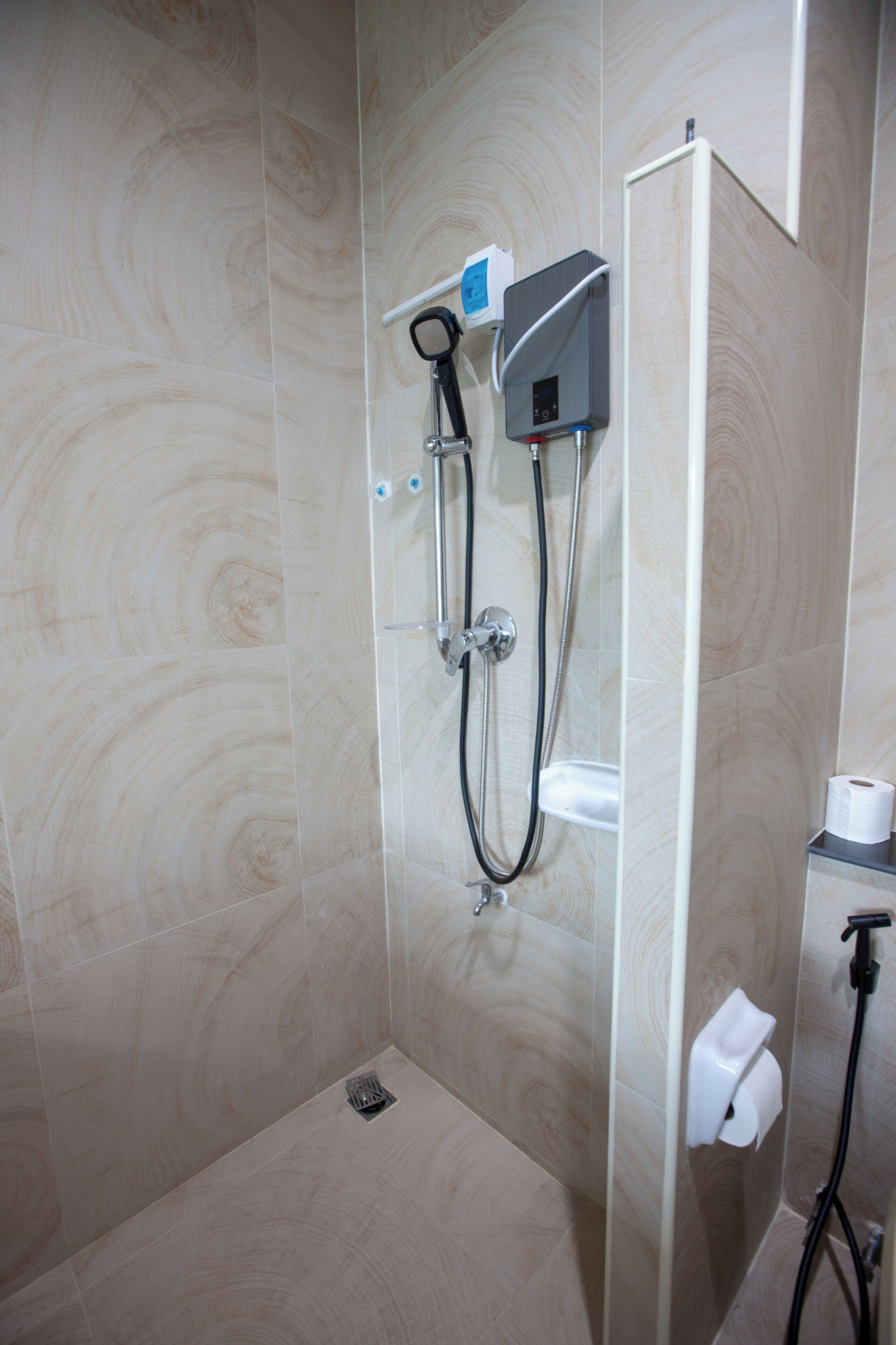 A shower area with a handheld showerhead, a wall-mounted control panel, and a toilet paper dispenser.