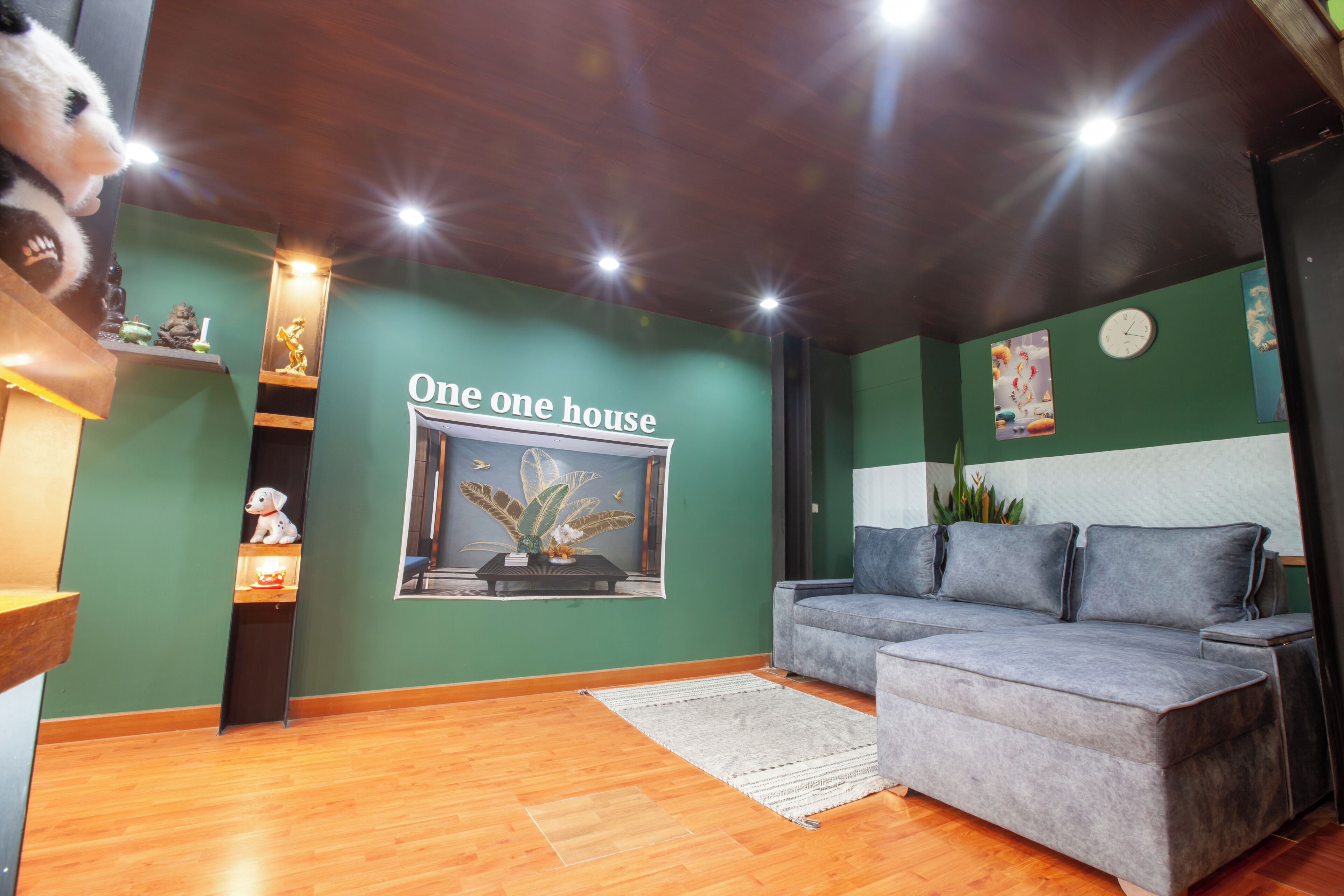 Ein Wohnzimmer mit grauem Sofa, Holzboden, einer grünen Akzentwand und einem Poster mit dem Text 'One one house'.