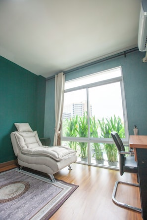 A room with a large window, a reclining chair, a desk, and a potted plant.