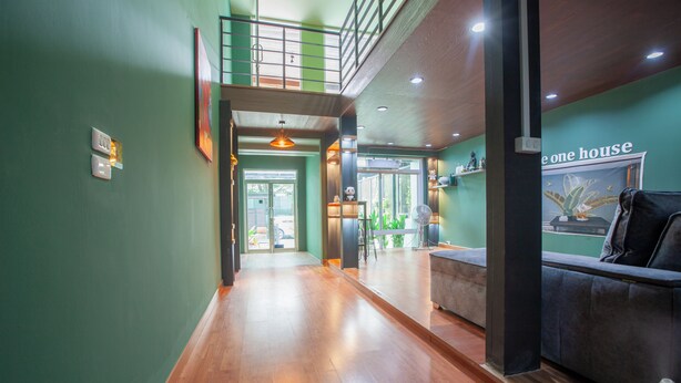 Un hall de hotel con piso de madera, un sofá, un ventilador y un cartel que dice 'one house'.