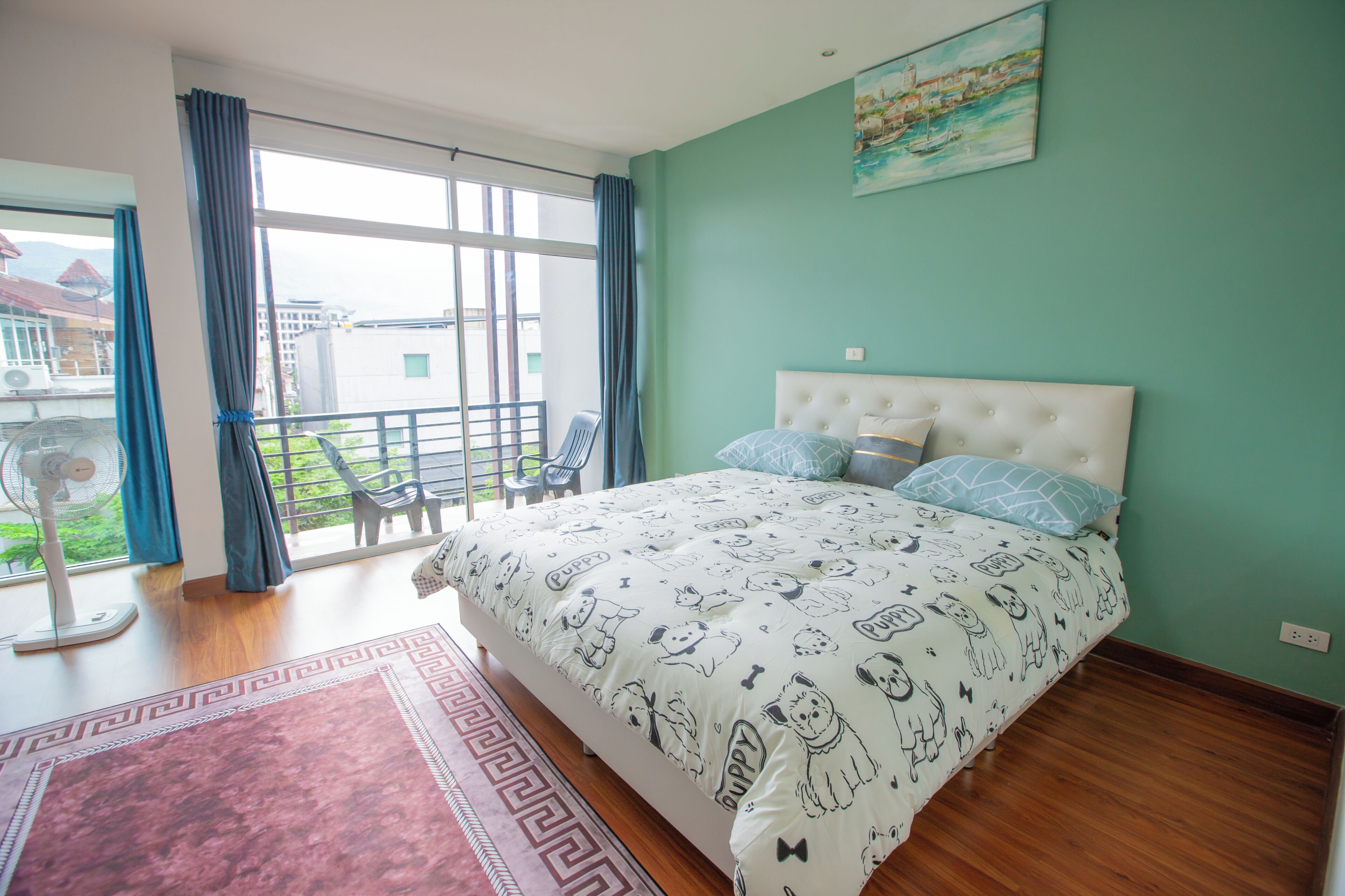 A bedroom with a large bed, a balcony with a view, and a painting on the wall.