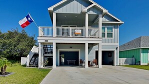 A two-story house with a balcony, a garage, and a flag. - Lone Star Lookout | Pet-Friendly + Community Pool! (Rockport)
