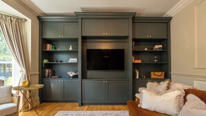 Ein Wohnzimmer mit einem dunklen Holzschrank, einem Flachbildfernseher und einem braunen Sofa.