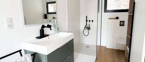 A modern bathroom with a white sink, dark grey cabinet, and a shower area.