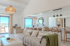 Ein geräumiger Wohnbereich mit großem Sofa, Esstisch und Stühlen, einem Balkon mit Aussicht und Pendelleuchten.
