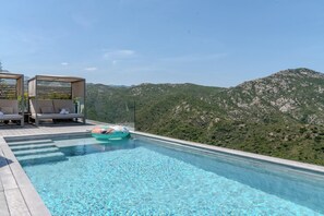 Ein Infinity-Pool auf dem Dach mit freiem Blick auf Berge, Liegestühle und eine Holzterrasse.