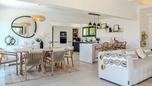 A modern living room with a dining area, kitchen, and a sofa with a patterned throw. - VILLA prestige ROYA vue mer à Saint Florent (Saint-Florent)