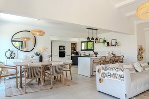 A modern living room with a dining area, kitchen, and a sofa with a patterned throw. - VILLA prestige ROYA vue mer à Saint Florent (Saint-Florent)
