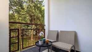 Ein Balkon mit Korbstuhl, einem Tisch mit Topfpflanze und Tasse, und Blick auf Bäume.