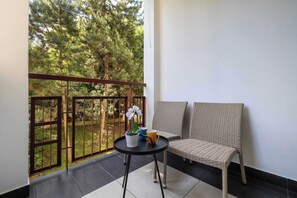 Ein Balkon mit Korbstuhl, einem Tisch mit Topfpflanze und Tasse, und Blick auf Bäume.
