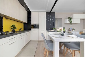 Une cuisine moderne avec des meubles blancs, un mur d’accent jaune et un coin repas comprenant une table blanche et des chaises grises.