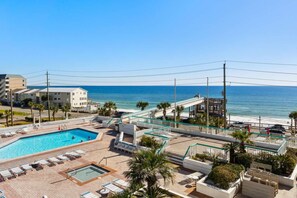 A rooftop pool area with a view of the ocean, lounge chairs, and a lifeguard tower. - "Summer Breeze" Beach Access, Beach Bar, Sky Bridge, Pool, Hot Tubs, Bonfires (Miramar Beach)