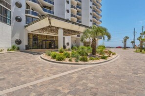 A modern hotel with a covered entrance, a landscaped garden, and a view of the ocean. - Summer Breeze, Beach, Beach Bar, Sky Bridge, Pool (Miramar Beach)