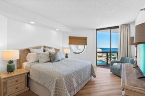 A hotel room with a bed, nightstands, a desk, a chair, a view of the ocean, and a balcony. - "Summer Breeze" Beach Access, Beach Bar, Sky Bridge, Pool, Hot Tubs, Bonfires (Miramar Beach)