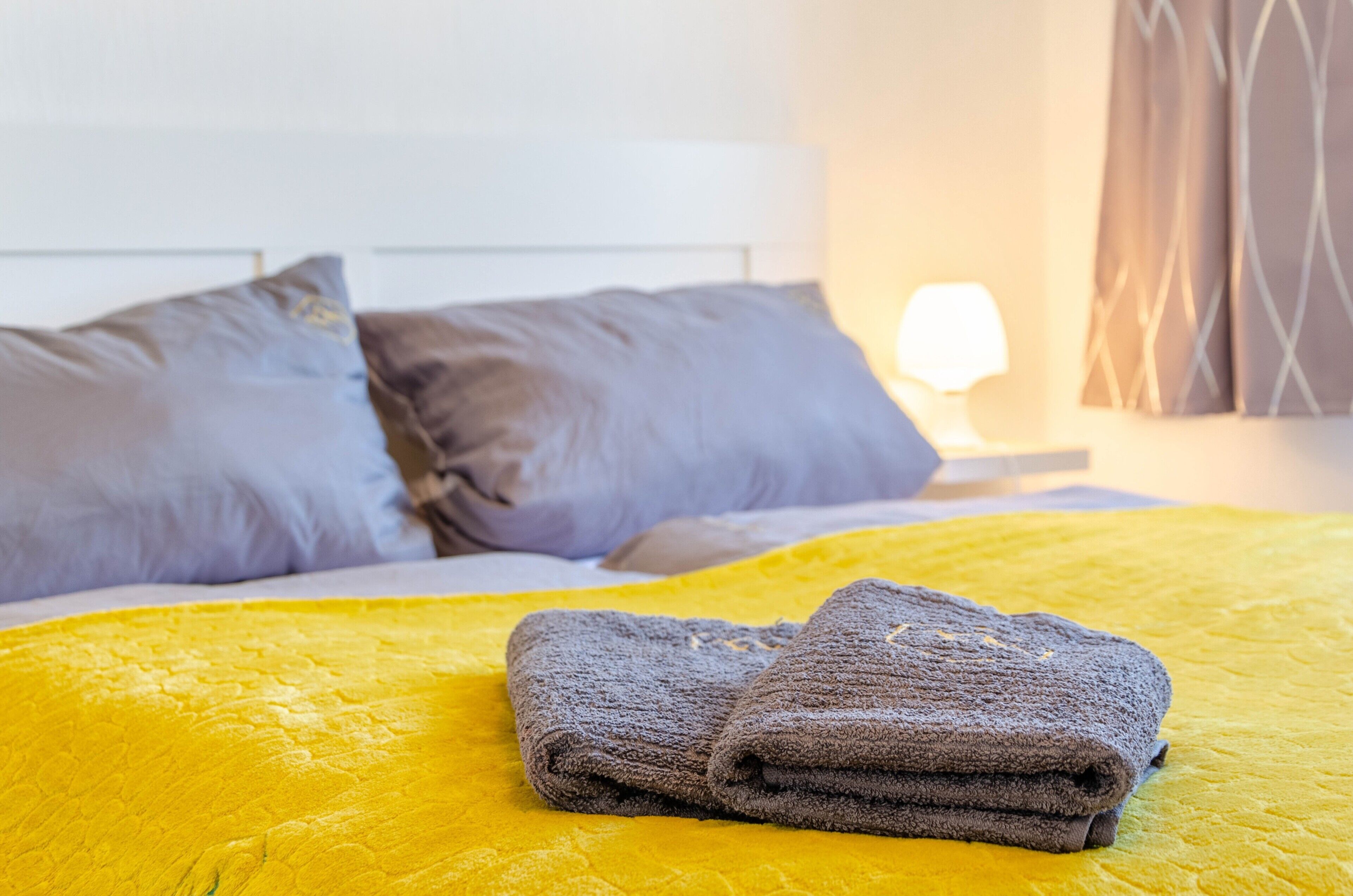 Una cama bien hecha con una colcha amarilla, dos almohadas y una toalla doblada.