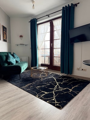 Una sala de estar con sofá, mesa de centro, televisor y ventana con cortinas.