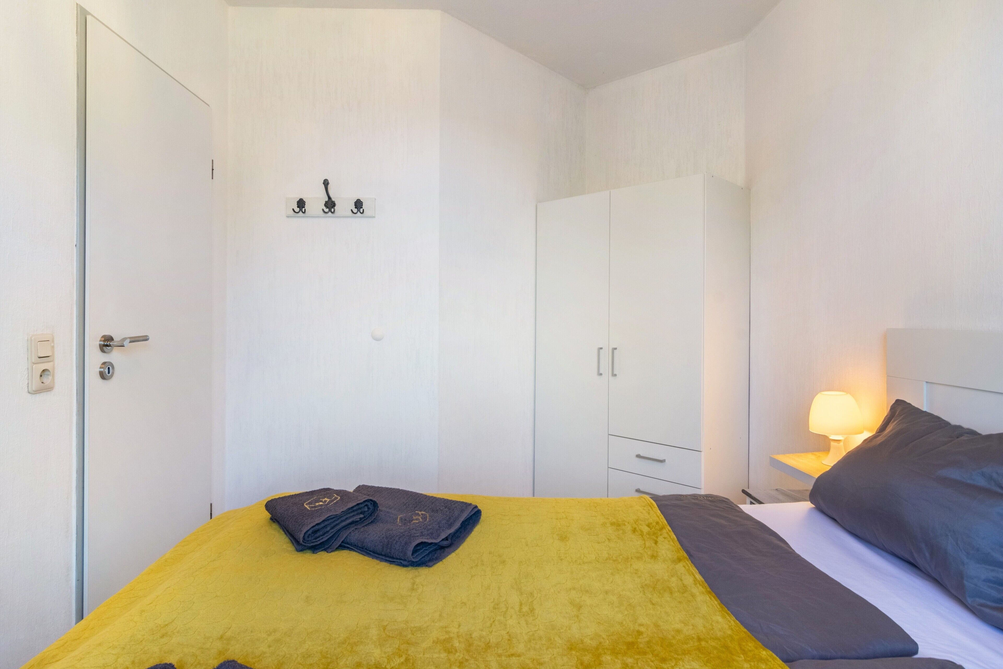 A bedroom with a bed, a nightstand, a lamp, and a wardrobe.