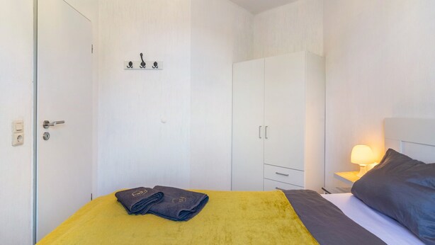 Un dormitorio con cama, mesita de noche, lámpara y armario.
