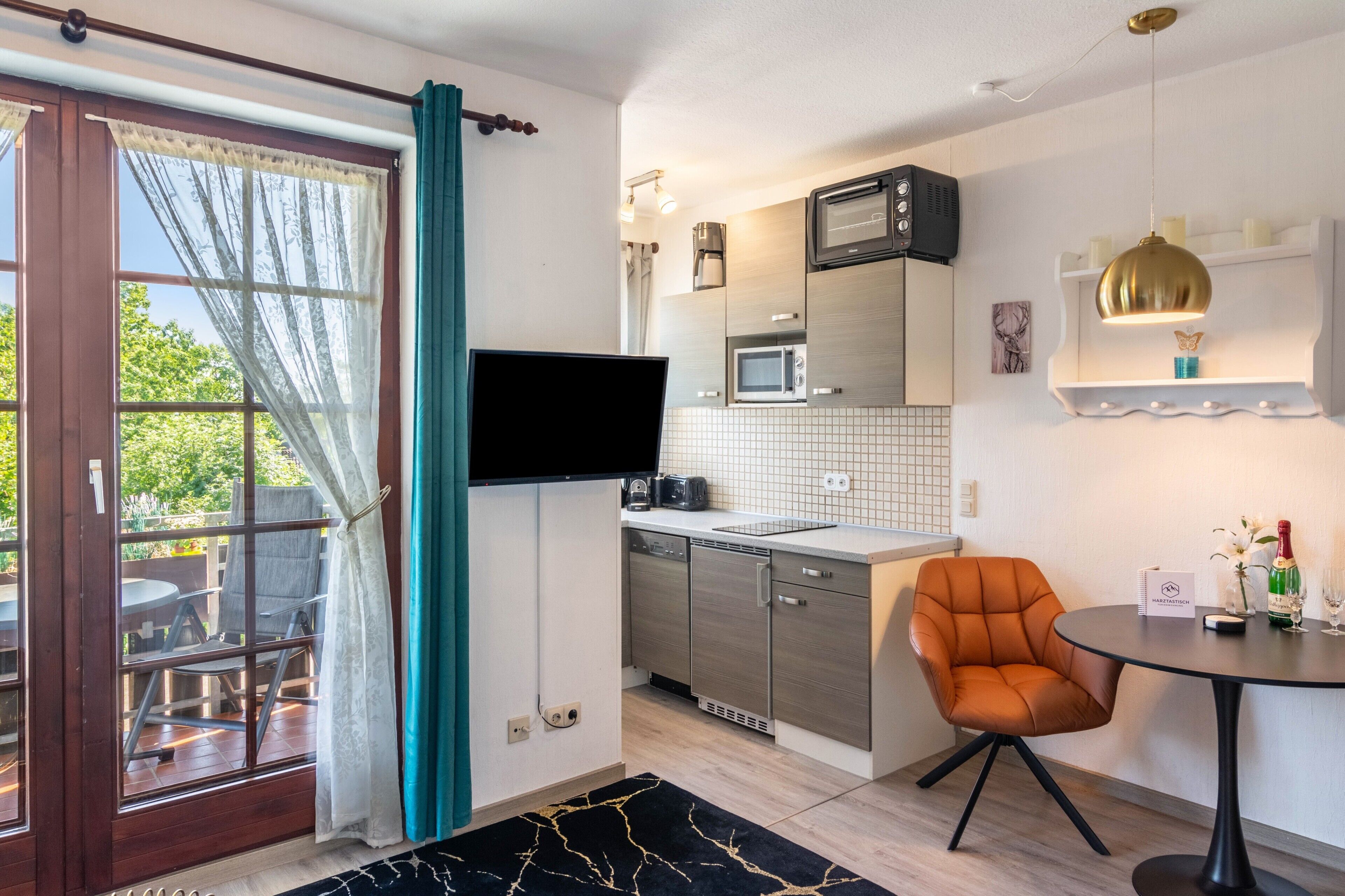 A compact kitchen with modern appliances, a flat-screen TV, and a dining area with a single chair.