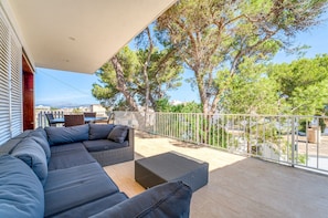 A balcony with a sectional sofa, wicker furniture, and a view of trees and buildings. - House with pool Can Quiros Can Picafort (Can Picafort)