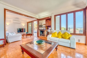 A spacious living room with a fireplace, a white sofa with yellow cushions, and large windows offering a view. - House with pool Can Quiros Can Picafort (Can Picafort)