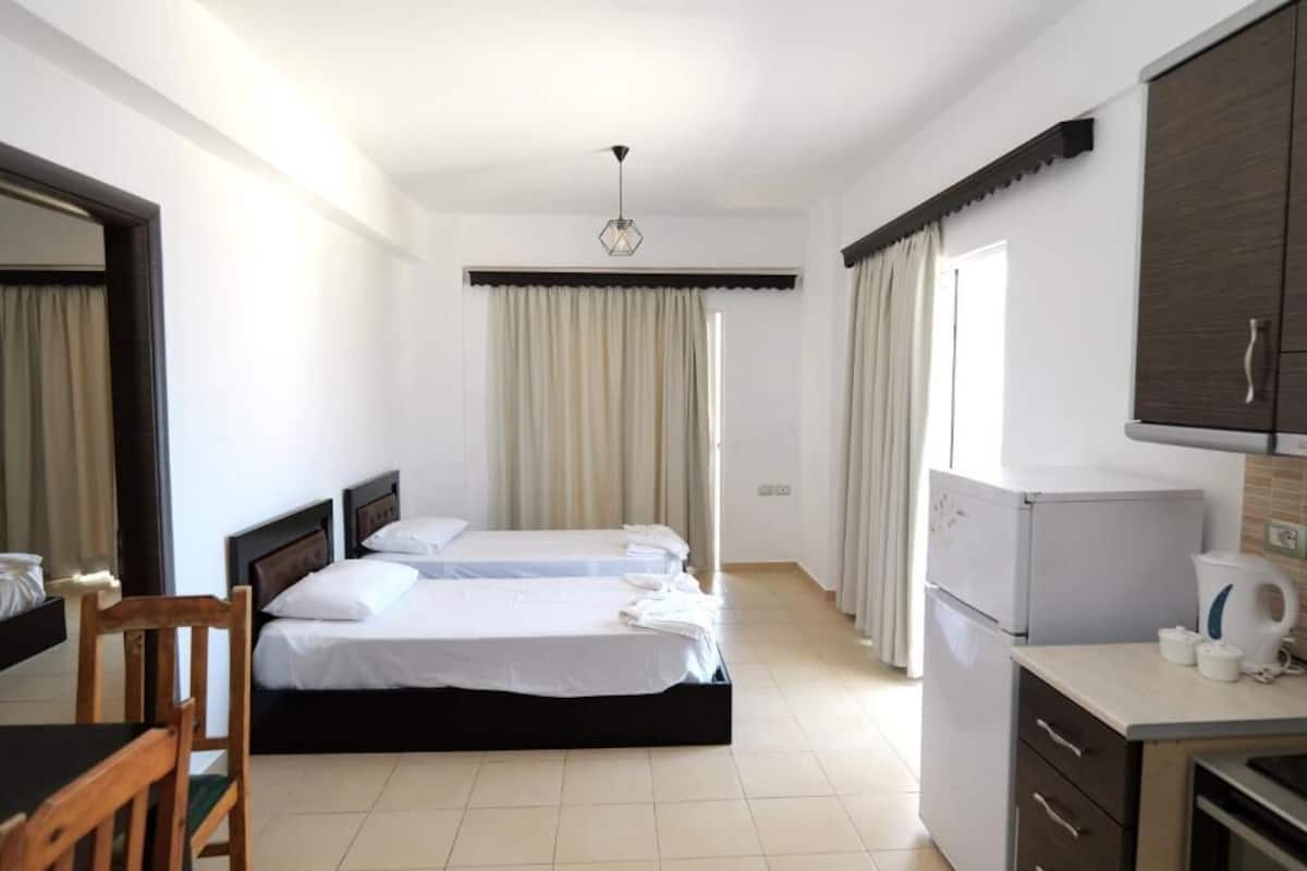 Habitació d'hotel amb dos llits, escriptori, nevera i finestra amb cortines.