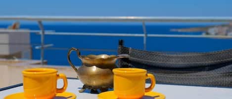 Una mesa con dos tazas amarillas y un hervidor de peltre, frente a una vista del océano azul.