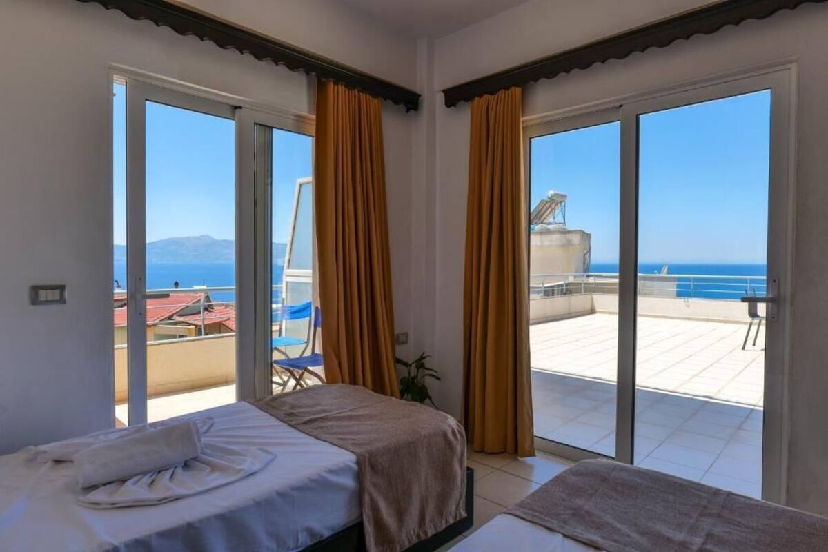 Habitació d'hotel amb un llit, una taula petita i vista al mar a través de grans portes corredisses.