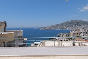 A coastal cityscape with buildings, a clear blue sea, and a distant mountain. - Fenix ApartHotel (Sarande)