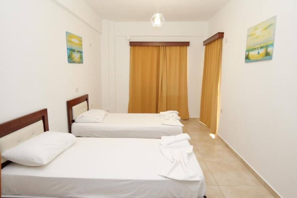 Habitació d'hotel amb dos llits, un amb capçalera de fusta, una làmpada al sostre i vista al passadís.