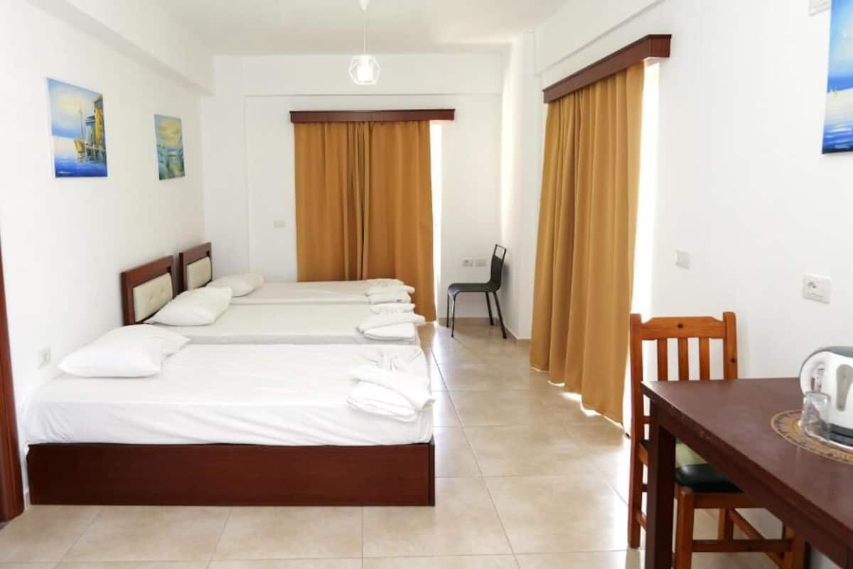 Una habitació d'hotel amb tres llits, una taula de menjador i una cadira.