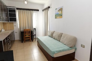A compact room with a bed, a desk, a chair, a window with curtains, a sink, and a cabinet.