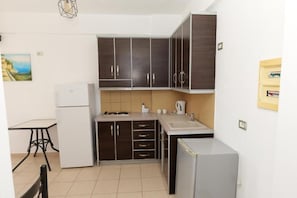 A compact kitchen with dark cabinets, a small sink, a refrigerator, and a dining table.