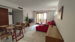 A living room with a red sofa, a glass dining table, and a TV. - Apartment in La Recoleta Punta Prima, Communal pools and steps away from the sea (Punta Prima)
