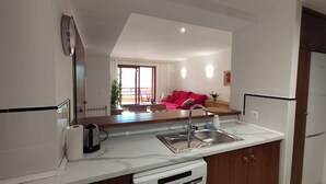 A kitchen with a sink, a coffee maker, and a toaster. There is a red couch in the background. - Apartment in La Recoleta Punta Prima, Communal pools and steps away from the sea (Punta Prima)