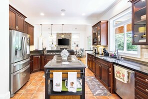 A modern kitchen with dark wood cabinets, stainless steel appliances, a central island with towels, and a large window providing natural light. - 5BR Gated Estate - Lake Views, Ping Pong (White)