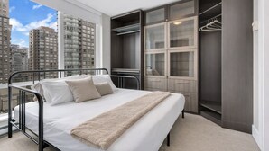 Een slaapkamer met een bed, een inloopkast en uitzicht op hoge gebouwen.