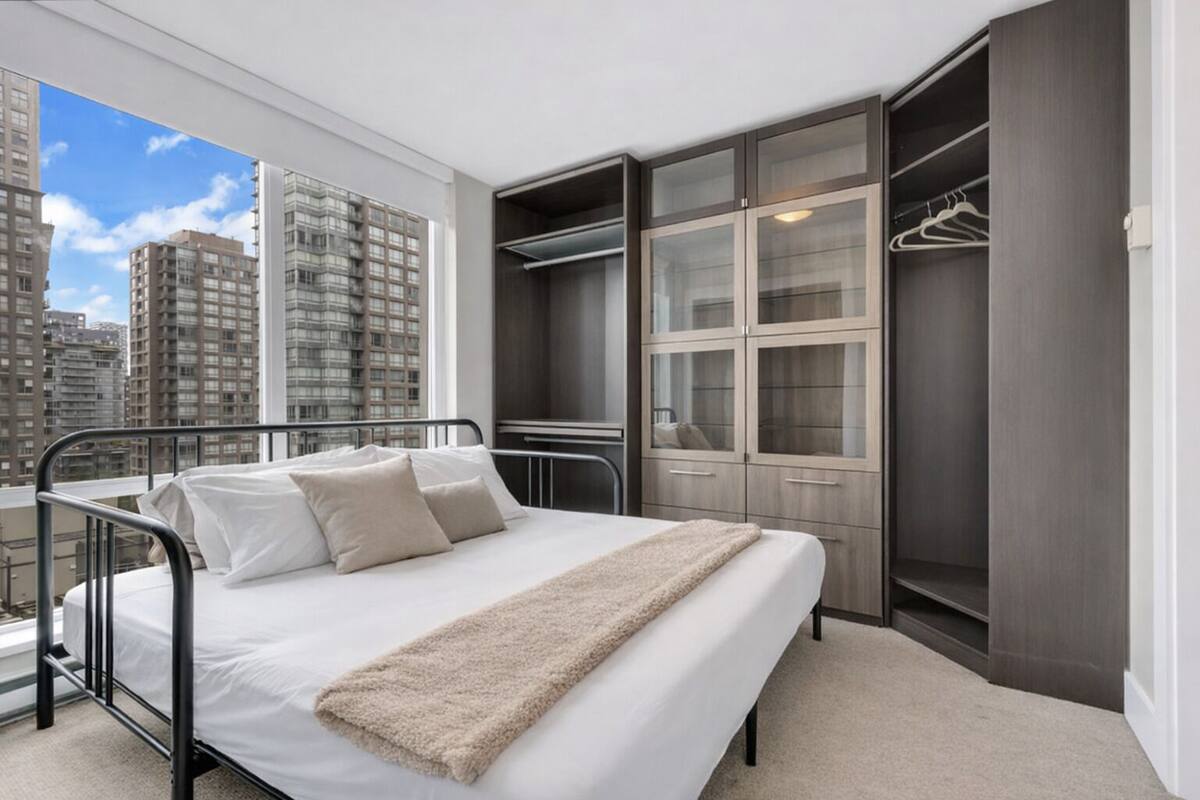 Quarto com cama, closet espaçoso e vista para edifícios altos.