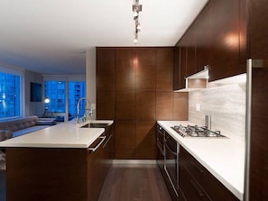 A modern kitchen with a central island, stainless steel appliances, and a view of the living area. - Modern Corner 2 BR with Spa (Vancouver)