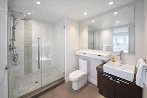A modern bathroom with a glass-enclosed shower, a toilet, a vanity with a sink, and a large mirror. - Modern Corner 2 BR with Spa (Vancouver)