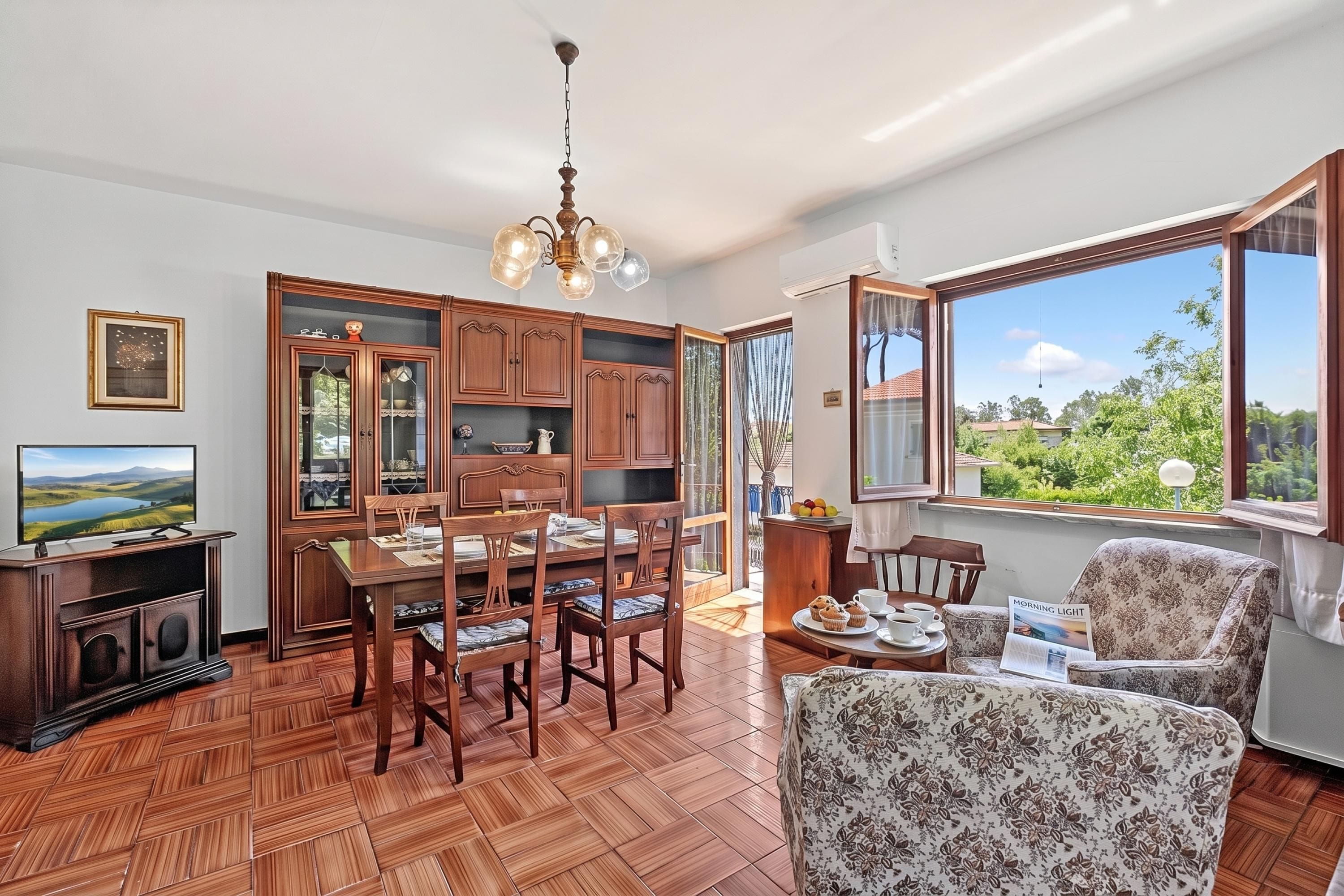A dining area with wooden furniture, a television, and a view of greenery outside.