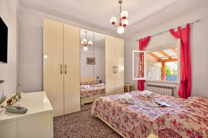 Ein Schlafzimmer mit Bett, Kleiderschrank, Schreibtisch, Spiegel und einem fensterbepflanzten Fenster.
