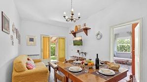 Un coin repas avec une table en bois dressée pour deux personnes, un canapé et un téléviseur fixé au mur.
