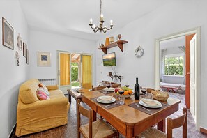 Ein Essbereich mit Holztisch für zwei Personen, einer Couch und einem Fernseher an der Wand.