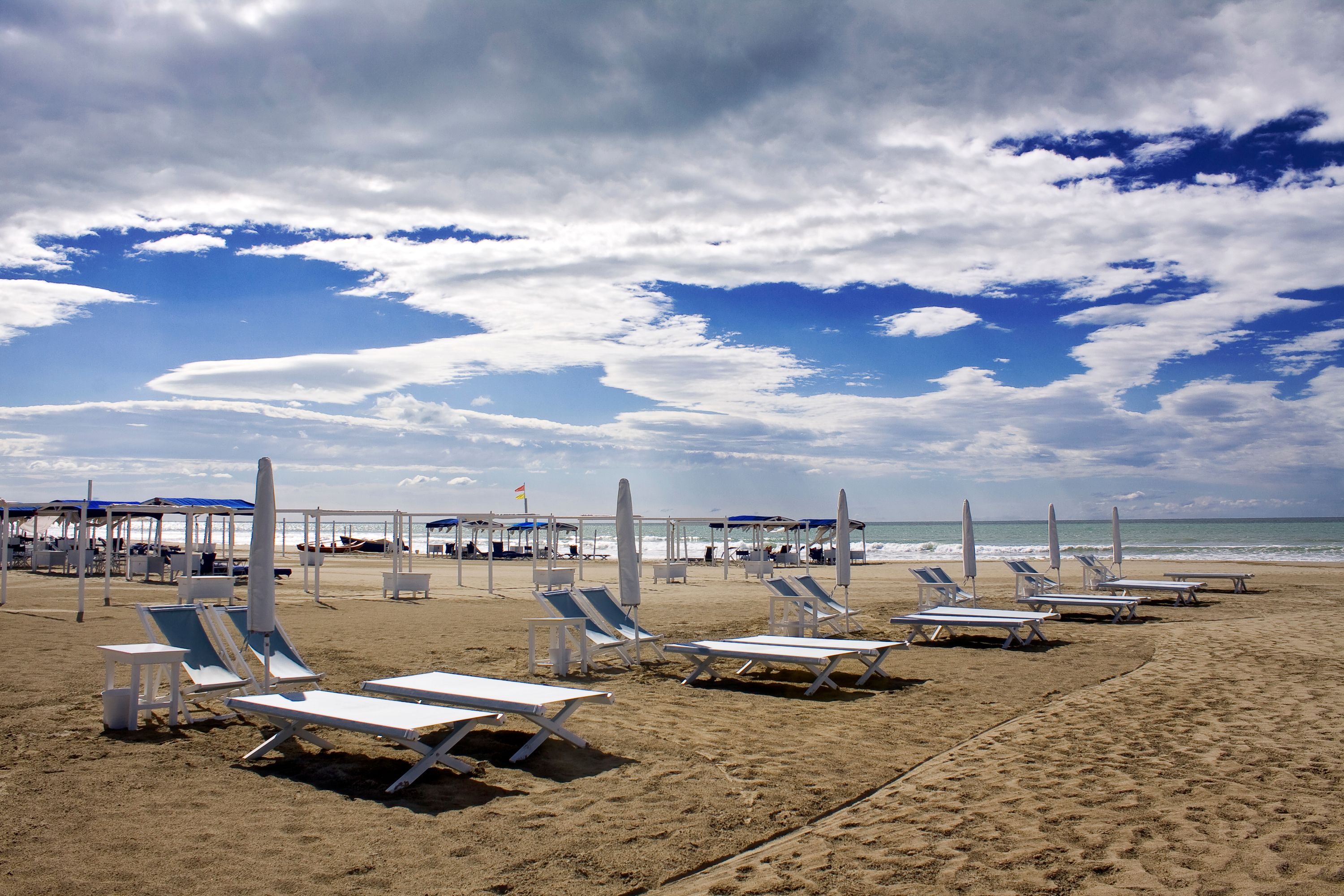 A beach with sun loungers and umbrellas, a clear sky, and the ocean in the background.