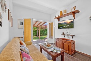 A living room with a sofa, coffee table, TV, wooden cabinet, and a door leading to a garden. - Casa Colombo With Garden In Forte Dei Marmi (Forte dei Marmi)