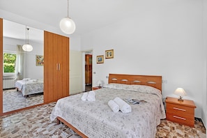A bedroom with a bed, wooden wardrobe, bedside table, lamp, and a mirror. - Casa Colombo With Garden In Forte Dei Marmi (Forte dei Marmi)